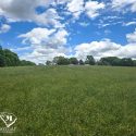 Expansive green field with wildflowers under a bright blue sky, showcasing potential for multi-use development near Interstate 85.