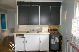 Kitchen area featuring dark cabinets, a sink, and a water heater, showcasing potential for renovation in a 2 bed, 1 bath home. Kitchen area featuring dark cabinets, a sink, and a water heater, showcasing potential for renovation in a 2 bed, 1 bath home.