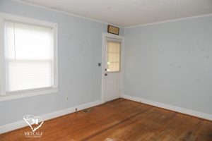 Bright, empty living room with hardwood floors, a door leading outside, and a window with blinds. Bright, empty living room with hardwood floors, a door leading outside, and a window with blinds.