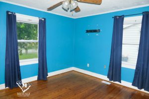 Bright blue room with hardwood floors, featuring two windows with dark curtains and a ceiling fan. Bright blue room with hardwood floors, featuring two windows with dark curtains and a ceiling fan.
