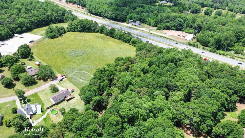 Aerial view of a multi-use property with open land and wooded areas adjacent to Interstate 85.