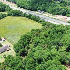 Aerial view of a multi-use property with open land and wooded areas adjacent to Interstate 85.