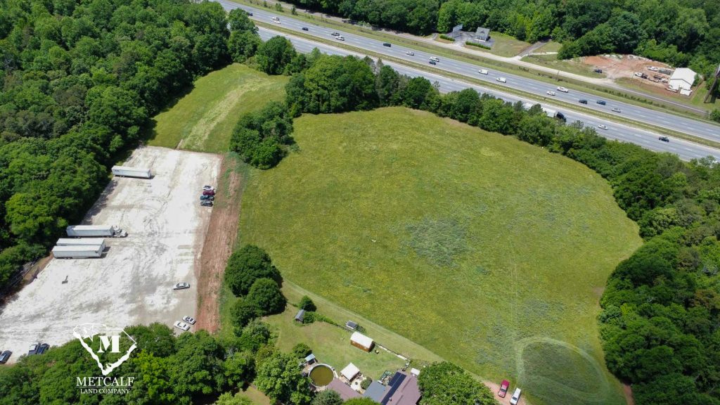 Aerial view of a multi-use property with open land and truck parking adjacent to Interstate 85, surrounded by greenery.