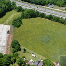 Aerial view of a multi-use property with open land and truck parking adjacent to Interstate 85, surrounded by greenery.