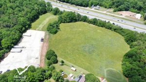 Aerial view of a multi-use property with open land and truck parking adjacent to Interstate 85, surrounded by greenery. Aerial view of a multi-use property with open land and truck parking adjacent to Interstate 85, surrounded by greenery.