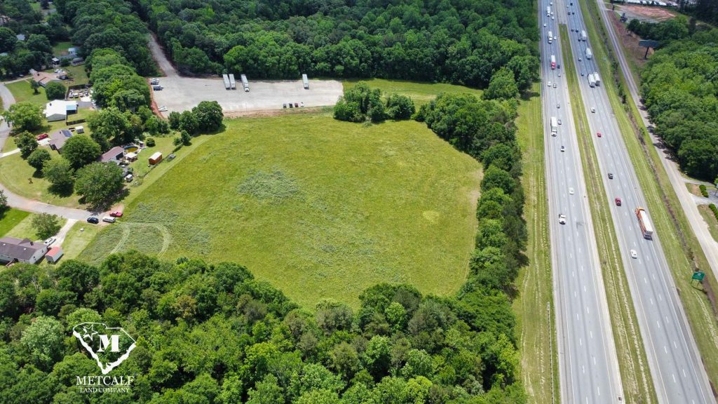 Aerial view of a multi-use property with open land adjacent to Interstate 85, surrounded by trees and nearby structures.