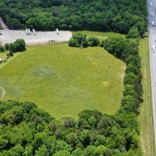 Aerial view of a multi-use property with open land adjacent to Interstate 85, surrounded by trees and nearby structures.