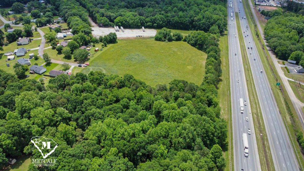 Aerial view of a multi-use property with open land adjacent to Interstate 85, surrounded by trees and residential areas.