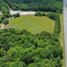 Aerial view of a multi-use property with open land adjacent to Interstate 85, surrounded by trees and residential areas.