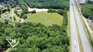 Aerial view of a multi-use property with green fields and trees adjacent to Interstate 85, showcasing potential development. Aerial view of a multi-use property with green fields and trees adjacent to Interstate 85, showcasing potential development.