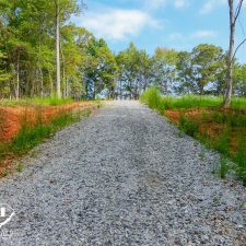 Gravel driveway leading through wooded area on a 2.5-acre homesite in Campobello, surrounded by greenery.