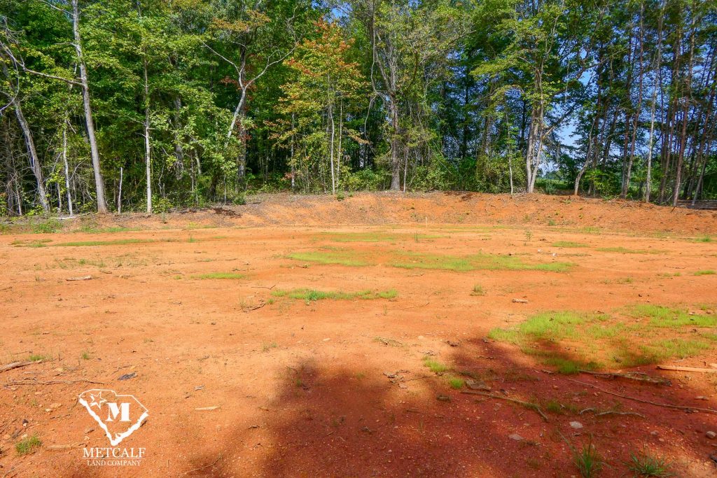 Cleared 2.5-acre homesite in Campobello, surrounded by trees and featuring red soil with patches of grass.