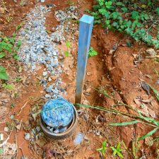 Water meter and marker on a 2.5-acre homesite in Campobello, surrounded by natural vegetation and gravel.